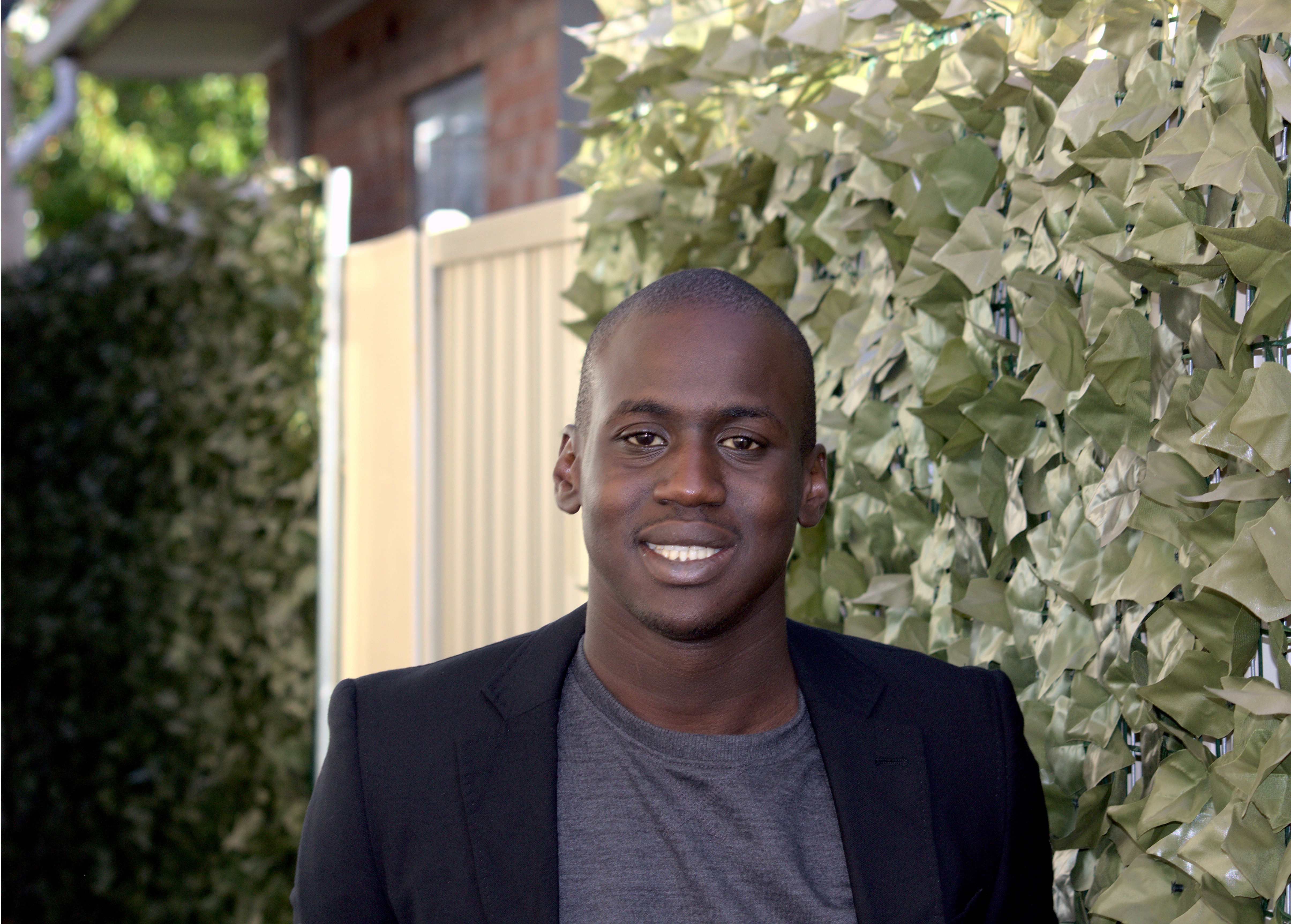 Picture of YNOT board member Joseph Akot smiling with the background of a hedge. 