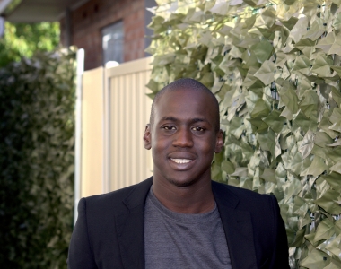Picture of YNOT board member Joseph Akot smiling with the background of a hedge. 